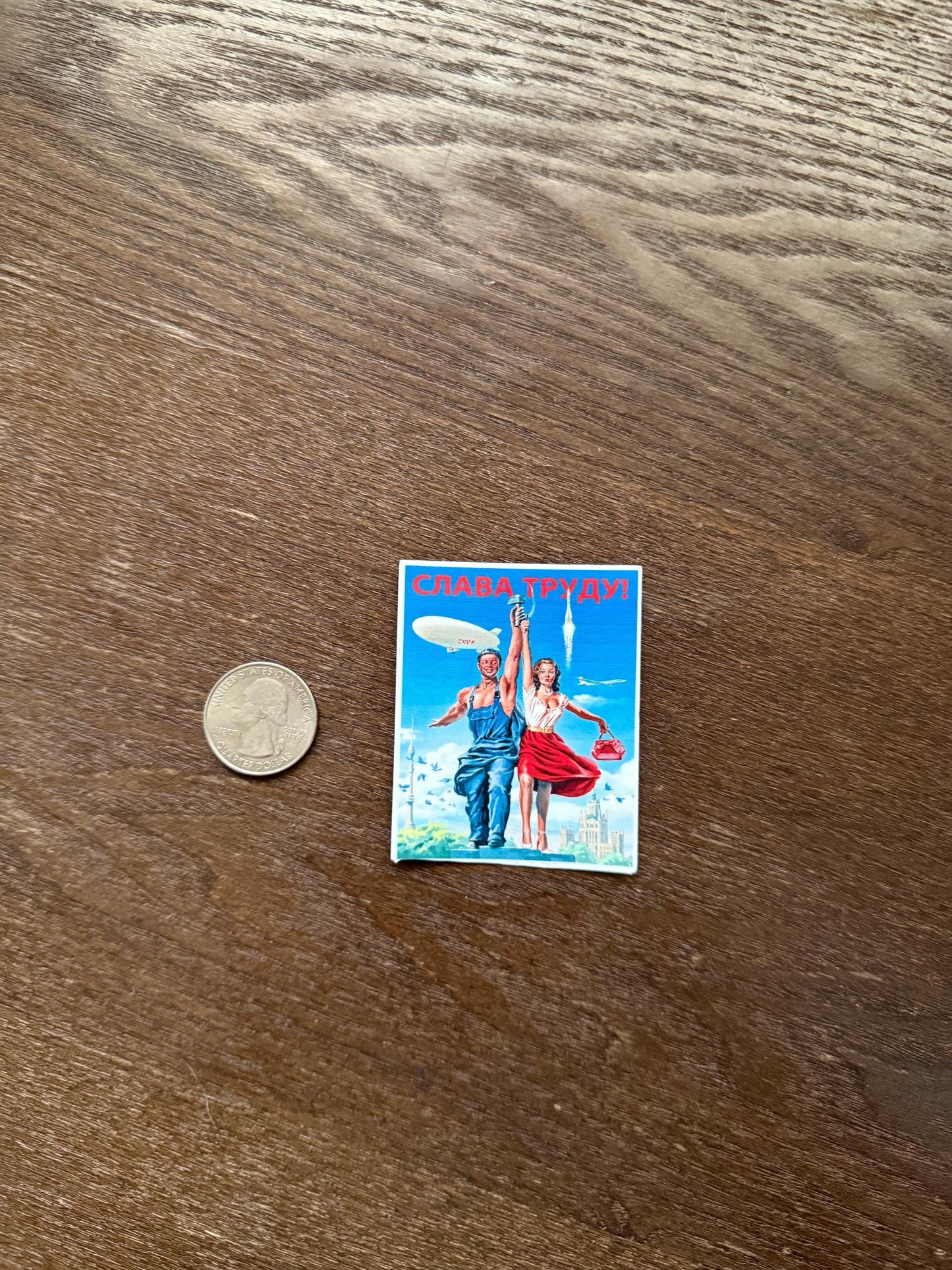 Small vintage-style poster on a wooden surface with a coin for scale