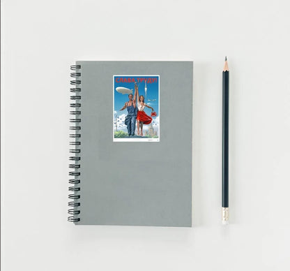 Gray notebook with a cover featuring a couple and a UFO, next to a black pencil on a light gray background