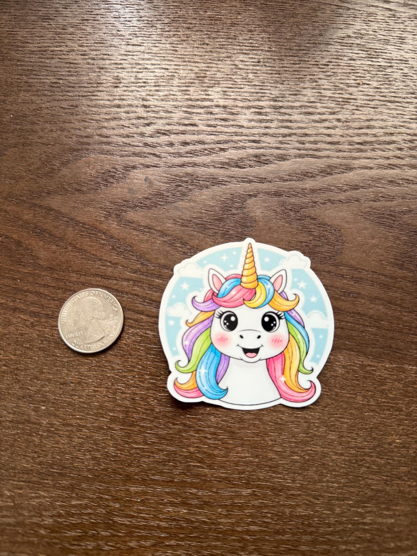 Sticker of a colorful unicorn with a coin for scale on a wooden surface