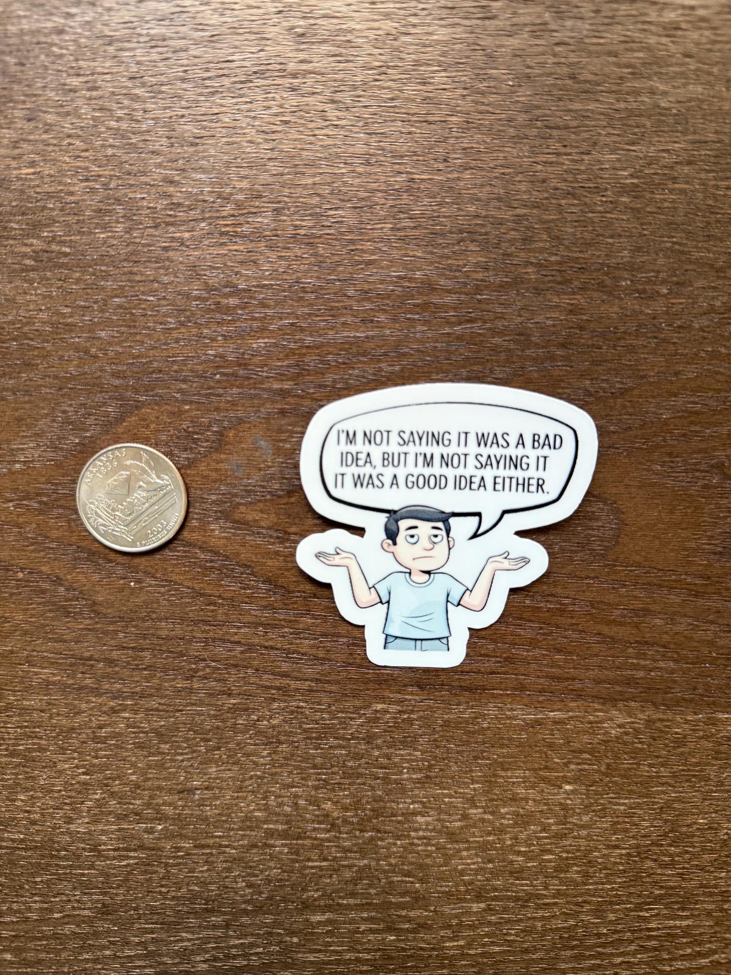 Sticker with a speech bubble and cartoon character on a wooden surface with a coin for scale.