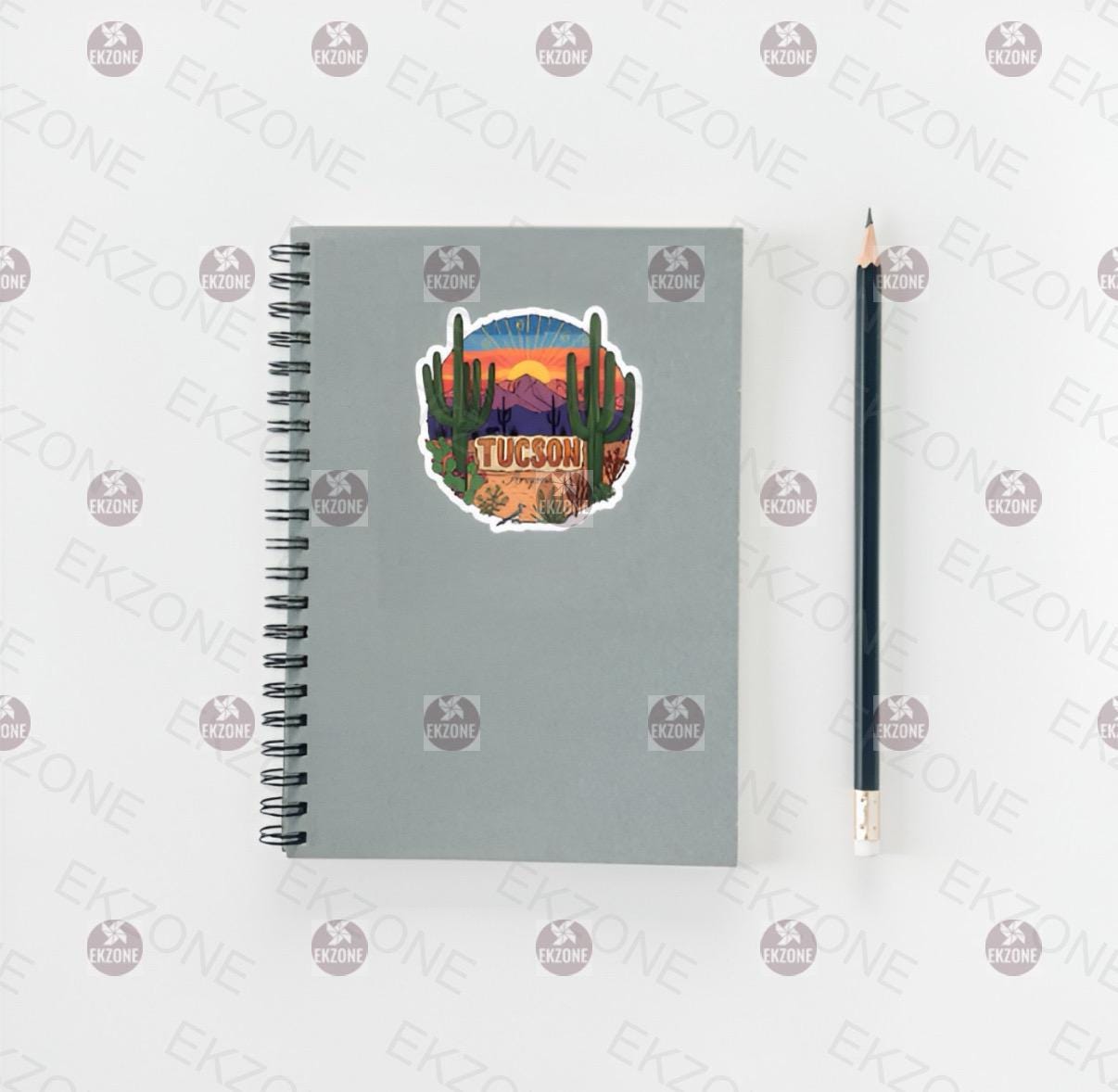 Gray spiral-bound notebook with a desert-themed sticker and a pencil on a white background.