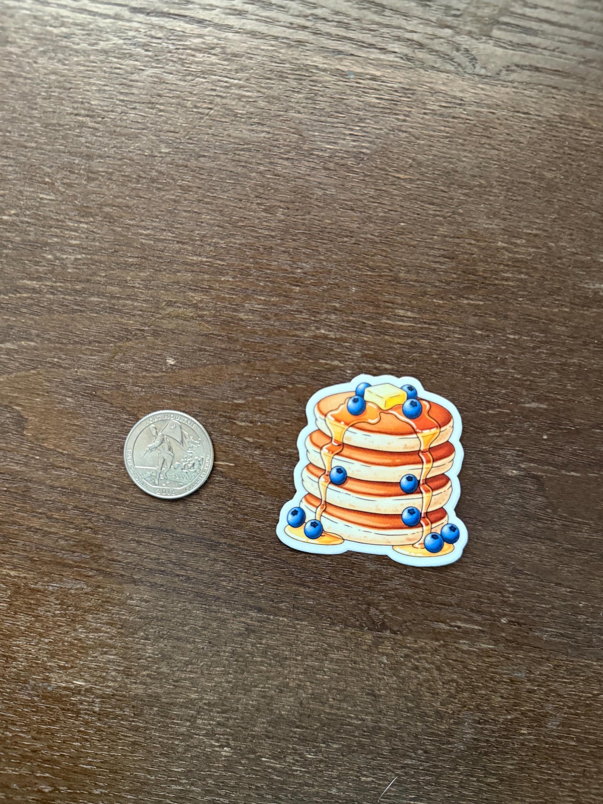 Stack of pancakes with blueberries sticker next to a coin on a wooden surface