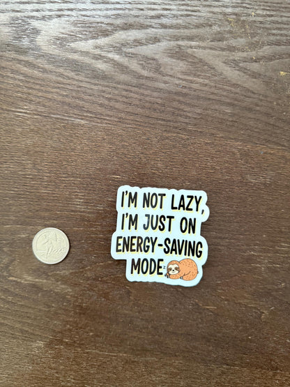 Sticker with text 'I'm not lazy, I'm just on energy-saving mode' on a wooden surface with a coin for scale.