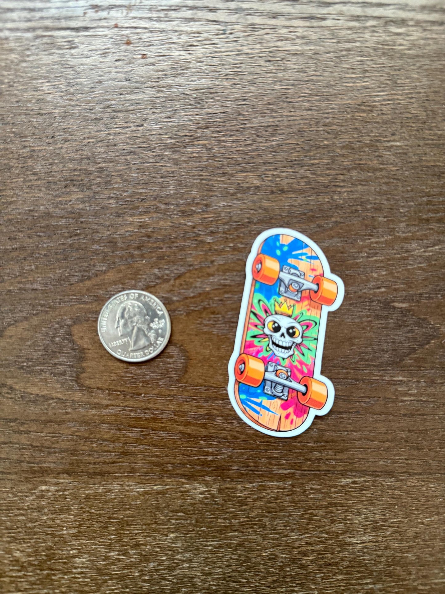 Colorful skateboard-shaped sticker with a skeleton design next to a quarter on a wooden surface