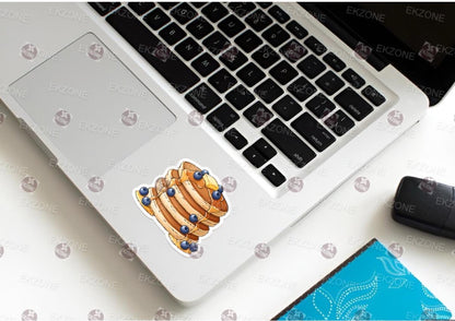 Laptop with a sticker of a bread loaf and blueberries on a white surface.