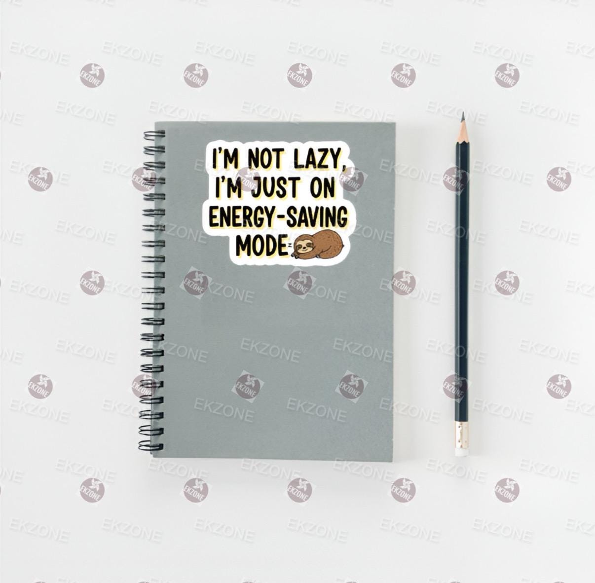 Notebook with a sticker saying 'I'm not lazy, I'm just on energy-saving mode' and a pencil on a white background