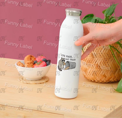 White water bottle with a design and text held by a hand on a wooden surface with a bowl of fruit and cookies.