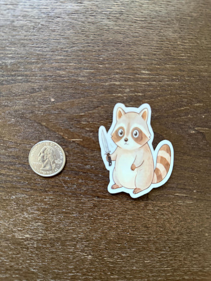 Sticker of a raccoon holding a butterfly next to a coin on a wooden surface