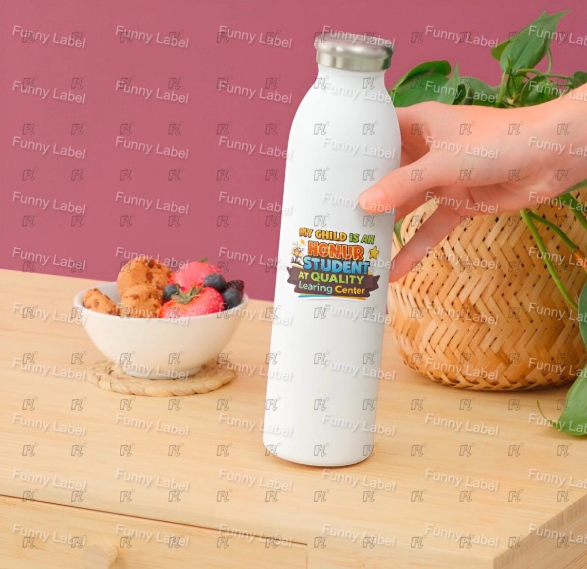 White water bottle with colorful label held by a hand on a wooden surface with a pink background.
