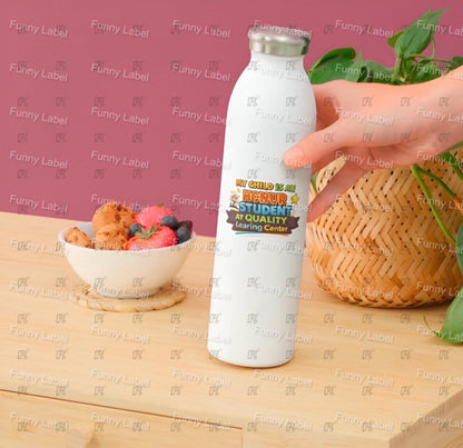 White water bottle with colorful label held by a hand on a wooden surface with a pink background.
