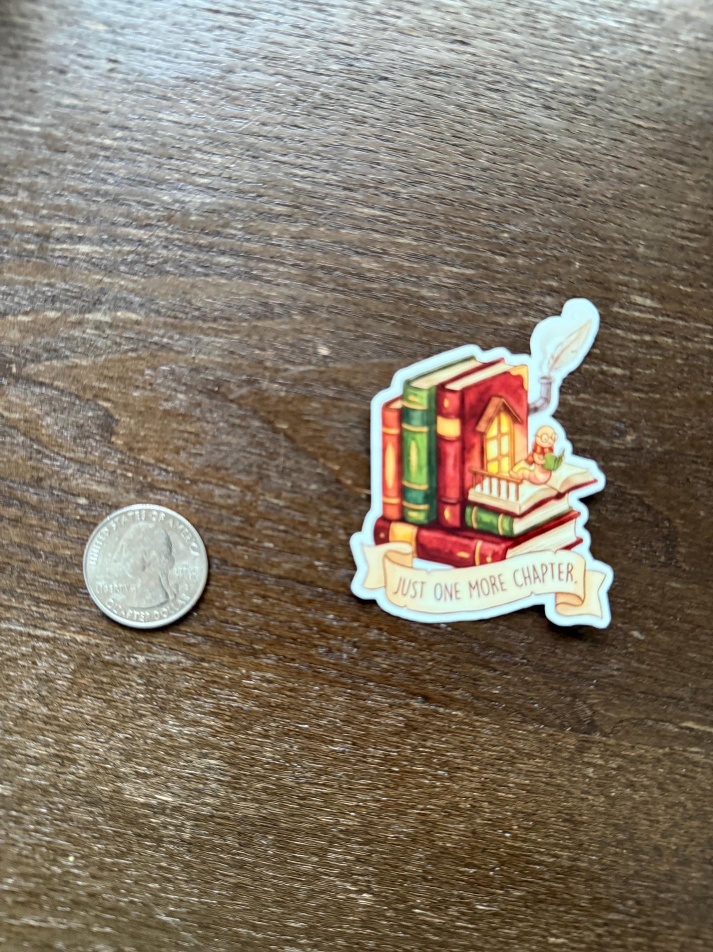 Sticker with books and a banner on a wooden surface next to a coin for scale.