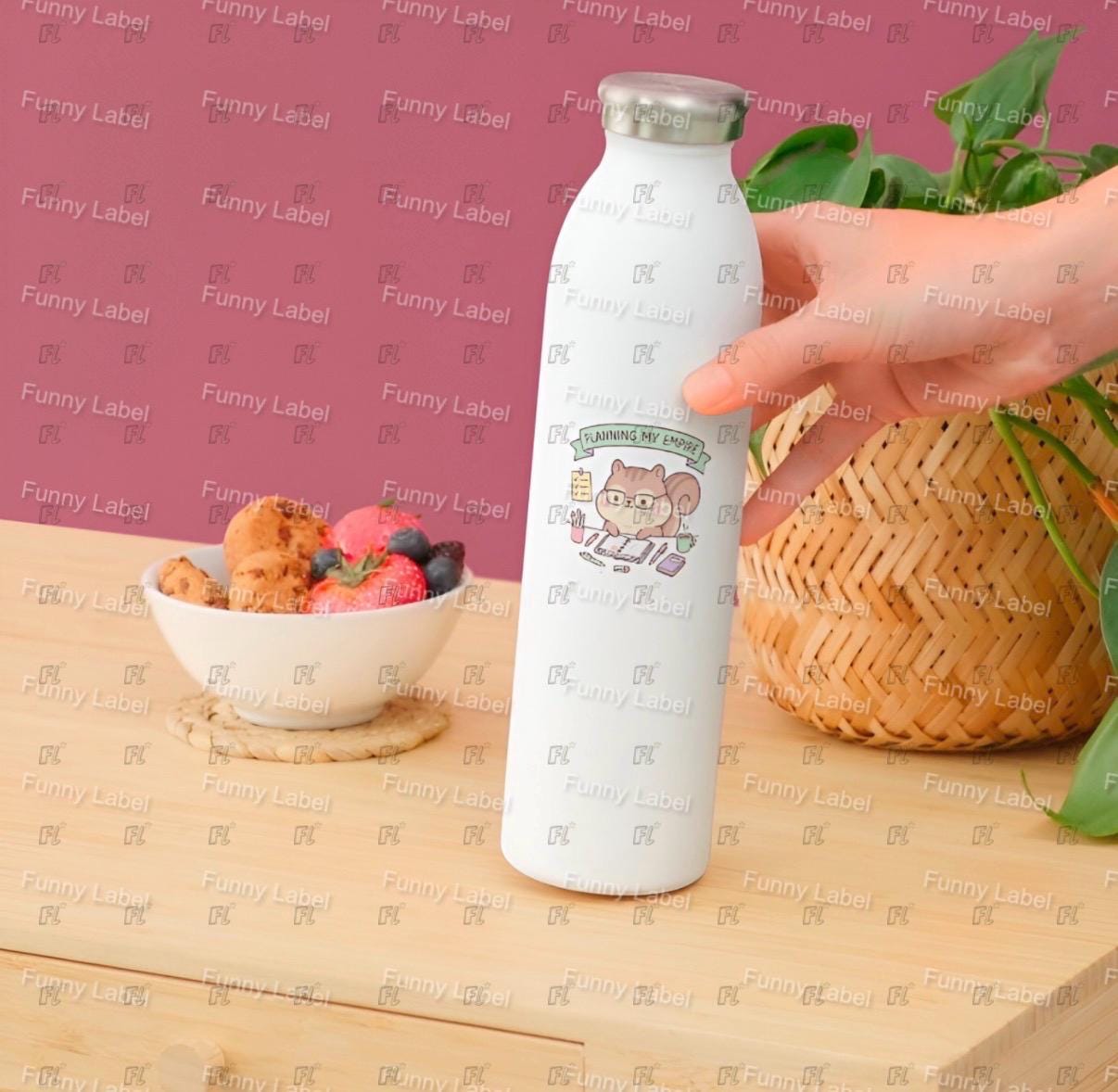 White water bottle with cartoon design held by a hand on a wooden table with a pink background.