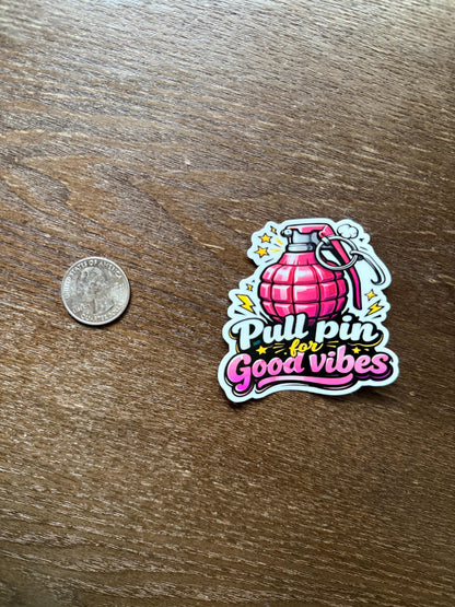 Sticker with a pink grenade design and text 'Pull pin for good vibes' on a wooden surface next to a coin for scale.
