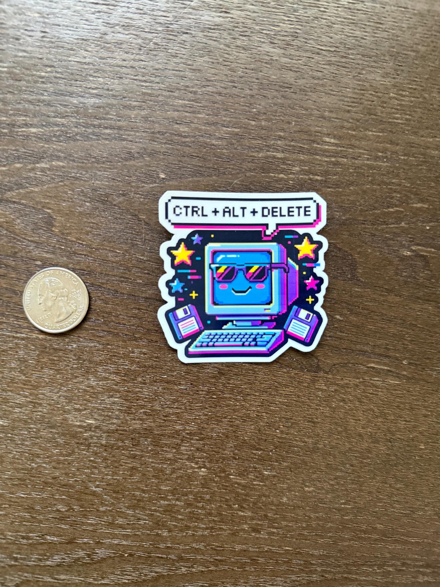 Sticker with a laptop design and 'CTRL + ALT + DELETE' text on a wooden surface with a coin for scale.