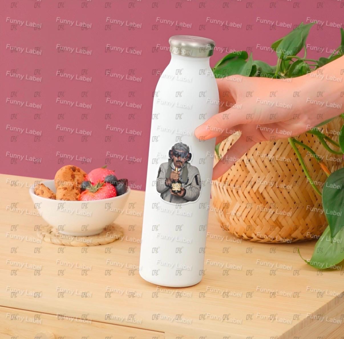 White water bottle with a printed design held by a hand on a wooden surface with a bowl of fruit and a basket.