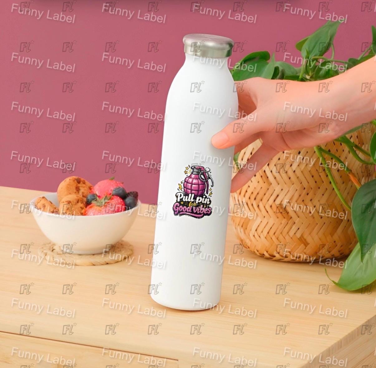 White water bottle with a colorful label held by a hand on a wooden table with a pink background.