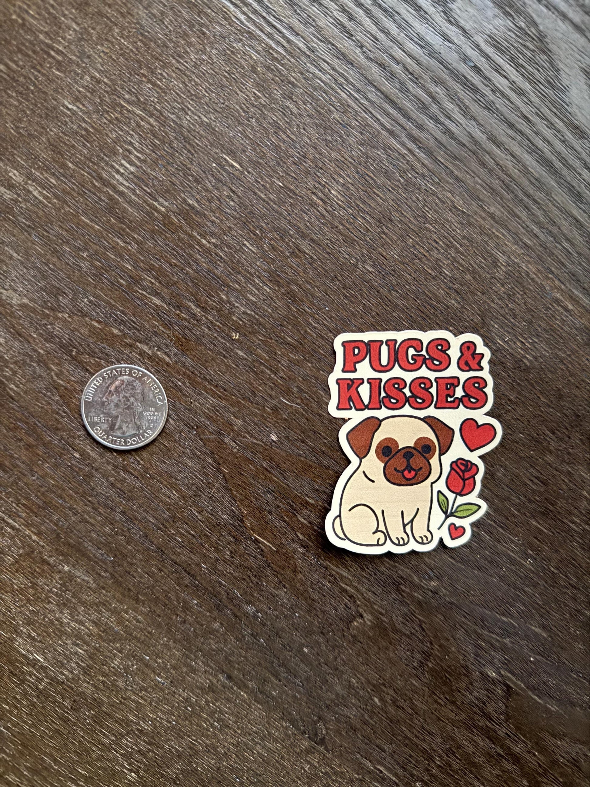 Sticker with a pug design and text 'Pugs & Kisses' on a wooden surface next to a coin for scale.