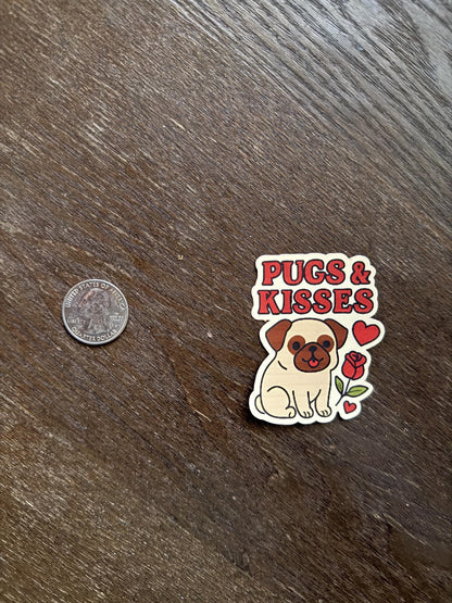 Sticker with a pug design and text 'Pugs & Kisses' on a wooden surface next to a coin for scale.
