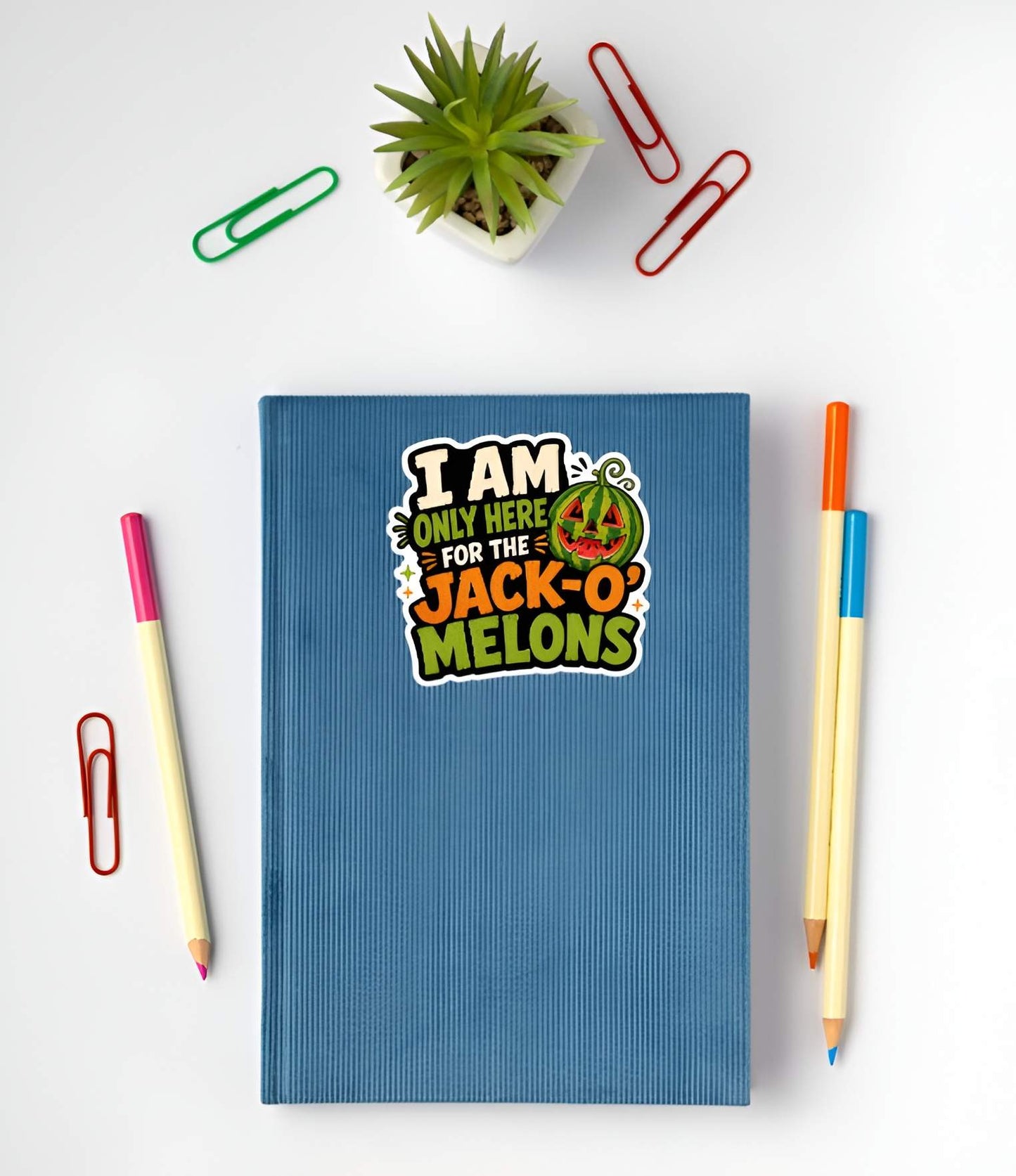 Blue notebook with a Funny Summerween watermelon stickeron a white surface with stationery items.